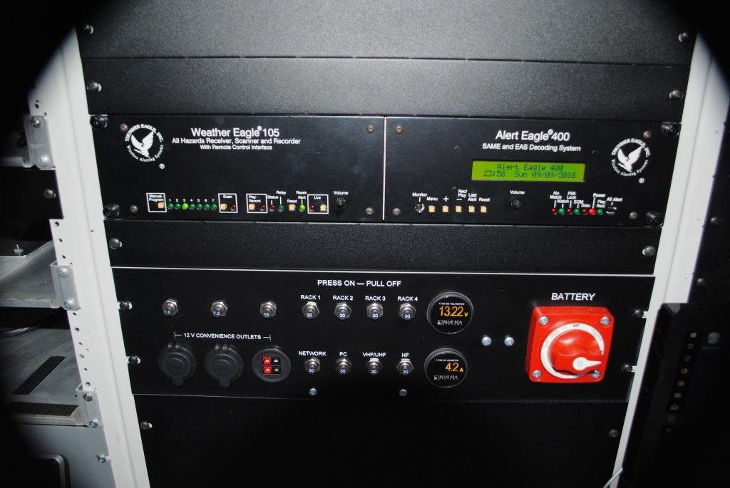 Close-up of a weather radio and DC power panel containing circuit breakers, meters, and the main DC power switch.